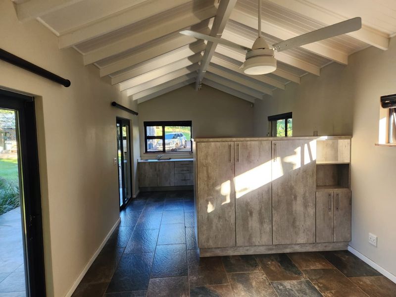 Open-plan living area featuring a vaulted ceiling, ceiling fan, tiled flooring, and built-in kitchen cabinetry with a sink.