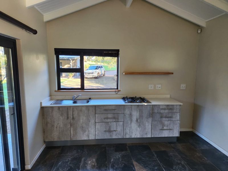 A modern, compact kitchen featuring concrete-look cabinetry, a gas hob, stainless steel sink, and vaulted ceilings, offering a clean and functional workspace.