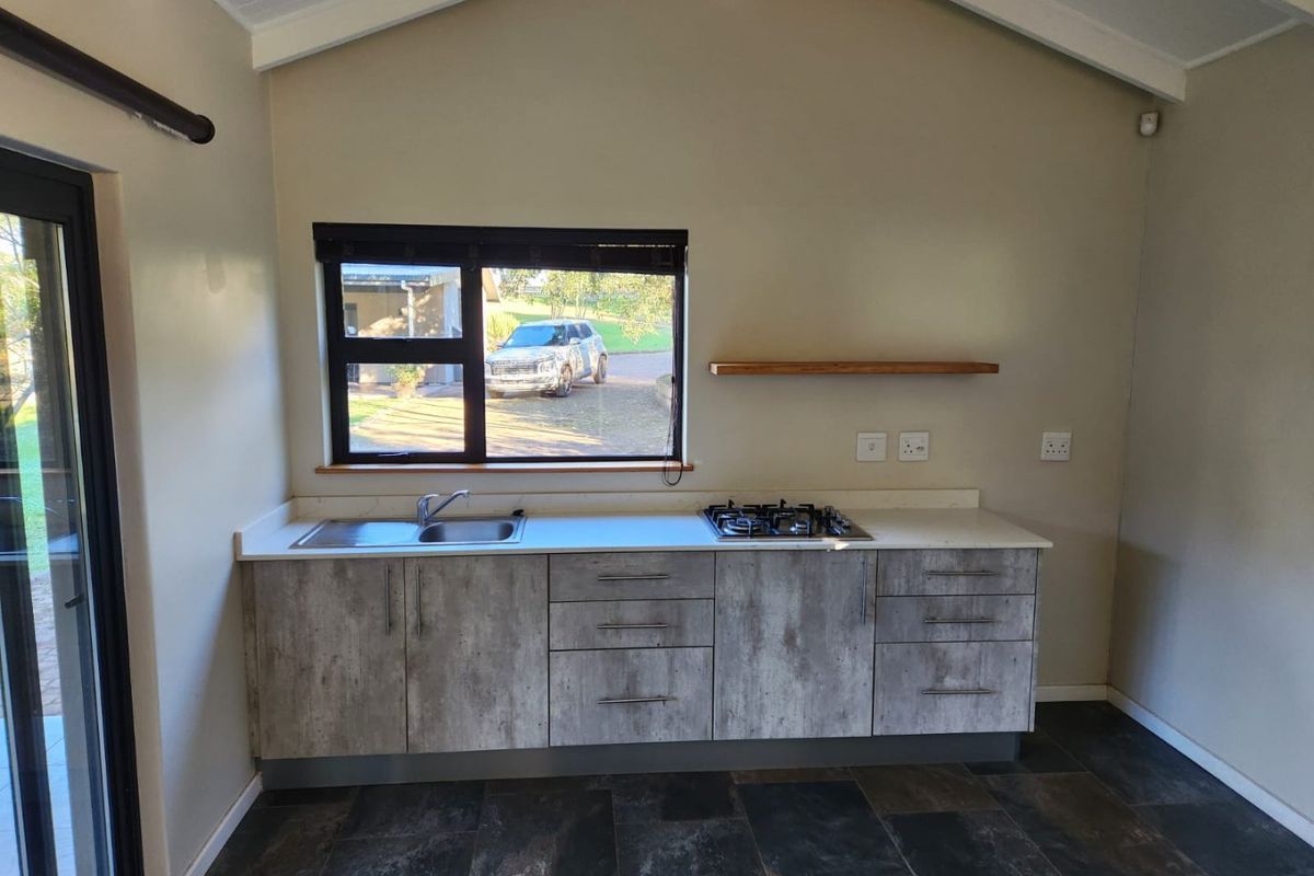 A modern, compact kitchen featuring concrete-look cabinetry, a gas hob, stainless steel sink, and vaulted ceilings, offering a clean and functional workspace.