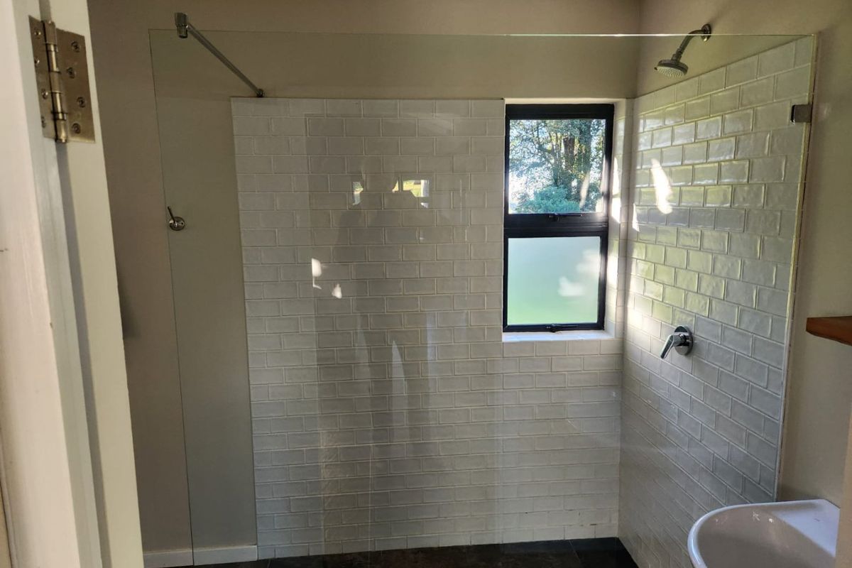 A modern bathroom featuring a walk-in shower with a glass screen, white subway tiling, and a pedestal basin.