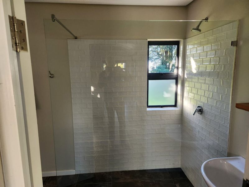 A modern bathroom featuring a walk-in shower with a glass screen, white subway tiling, and a pedestal basin.