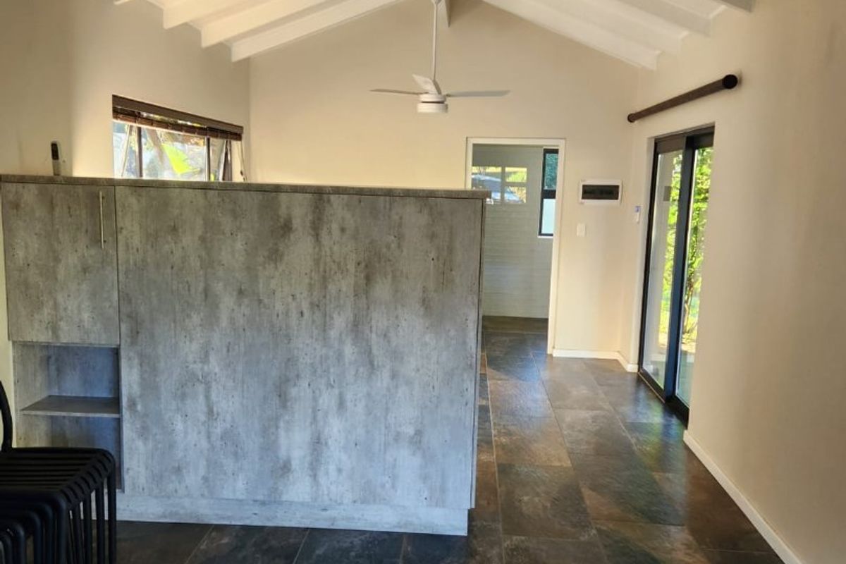 Spacious open-plan living area featuring vaulted ceilings with exposed rafters, slate tile flooring, and sliding glass doors leading to the exterior.