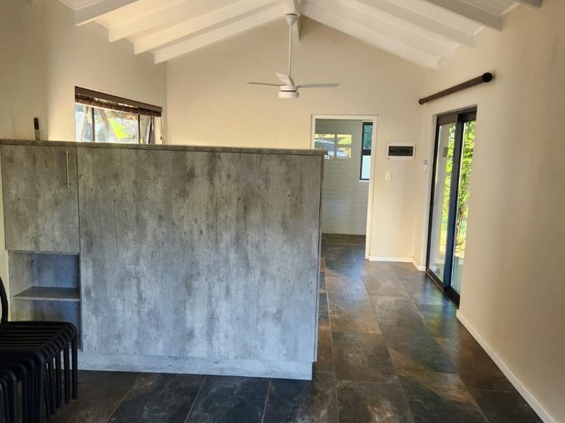 Spacious open-plan living area featuring vaulted ceilings with exposed rafters, slate tile flooring, and sliding glass doors leading to the exterior.