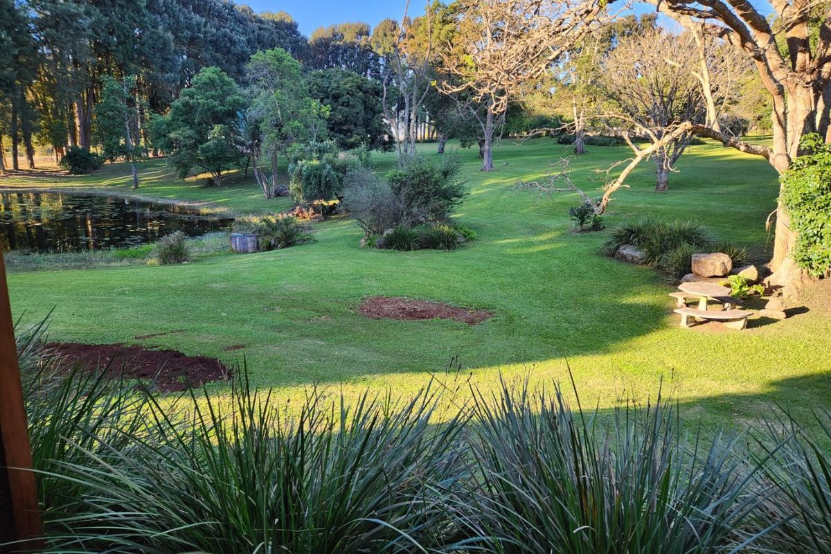 A spacious, well-maintained garden featuring a tranquil pond, mature trees, and expansive green lawns, offering a peaceful outdoor setting.
