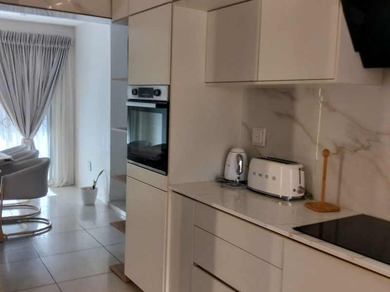 Modern kitchen featuring sleek handleless cabinetry, integrated oven, induction hob, and elegant marble-look splashback with neutral tiled flooring.