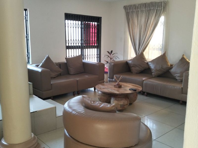 Spacious living room featuring neutral tiled flooring, recessed downlighting, and a prominent structural column, with access to the exterior via a security-gated sliding door.