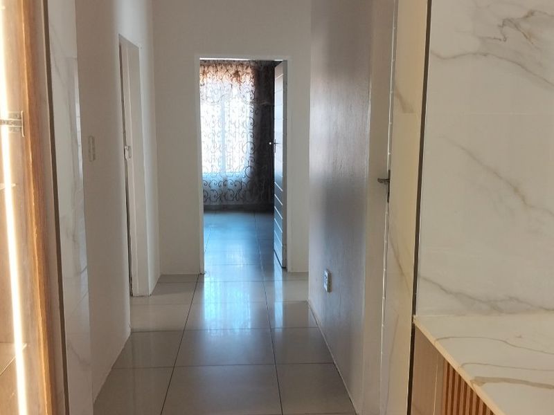 A bright, modern hallway featuring large-format floor tiles, marble-effect wall finishes, and clean, minimalist architectural lines leading through the home.