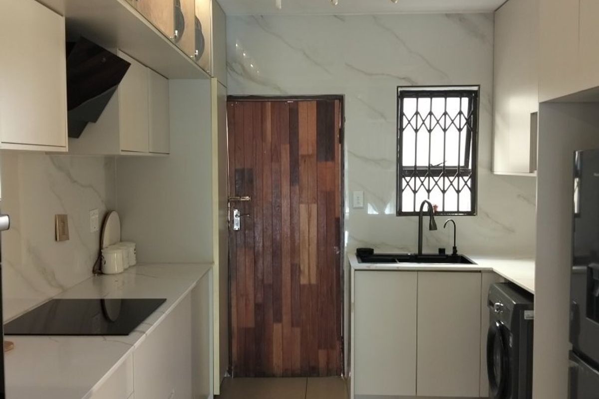 Modern galley-style kitchen featuring sleek white cabinetry, stone countertops, integrated induction hob, and high-quality finishes with ample storage and functional workspace.