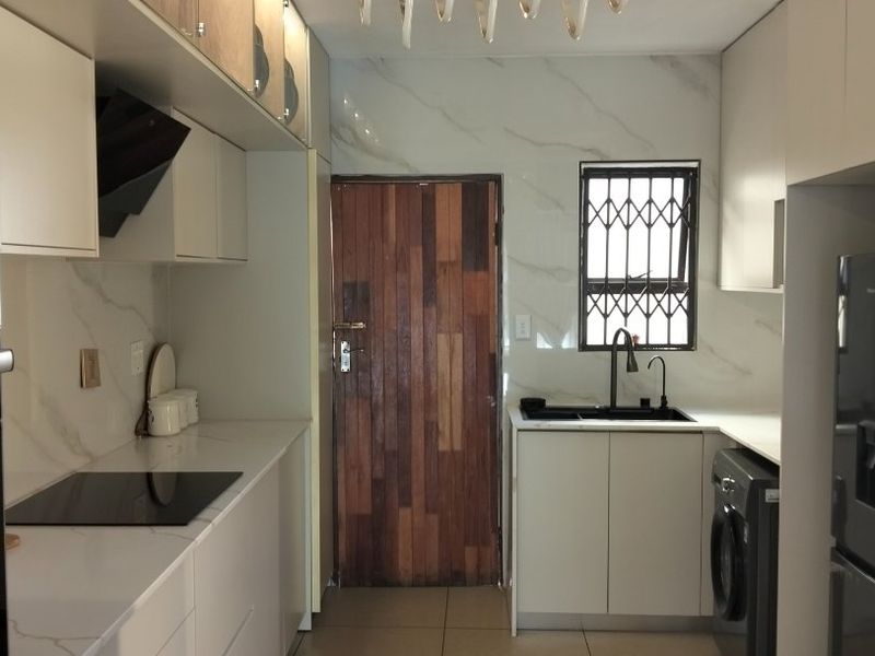 Modern galley-style kitchen featuring sleek white cabinetry, stone countertops, integrated induction hob, and high-quality finishes with ample storage and functional workspace.