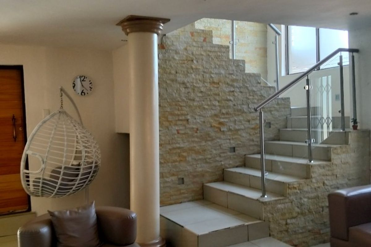 Spacious living area featuring a stone-clad staircase with glass balustrades, tiled flooring, and a prominent structural column.
