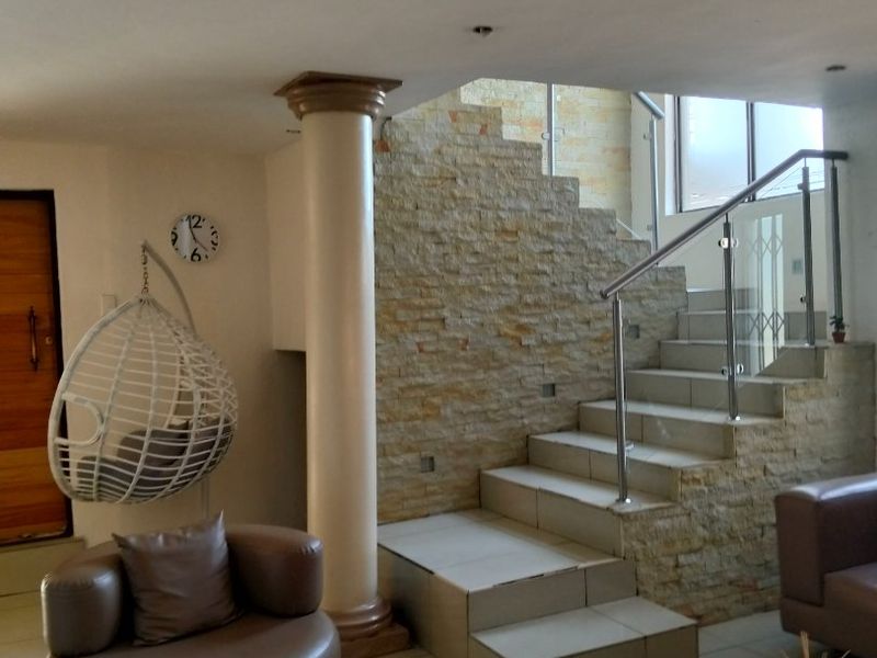 Spacious living area featuring a stone-clad staircase with glass balustrades, tiled flooring, and a prominent structural column.