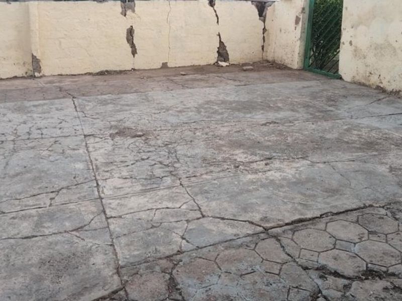 An outdoor rear area featuring a concrete paved surface and boundary walls, currently showing significant signs of wear and structural weathering.