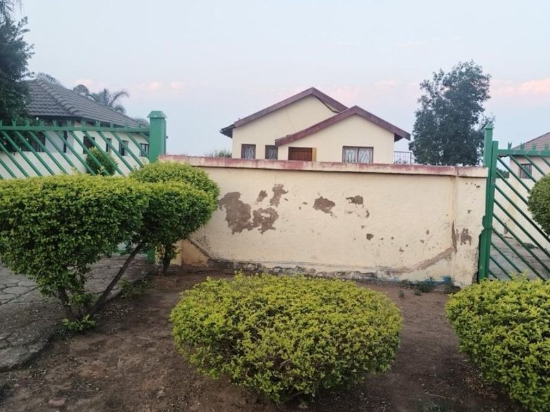 Front view of the property featuring a perimeter wall with security gate and a view of the main house structure.