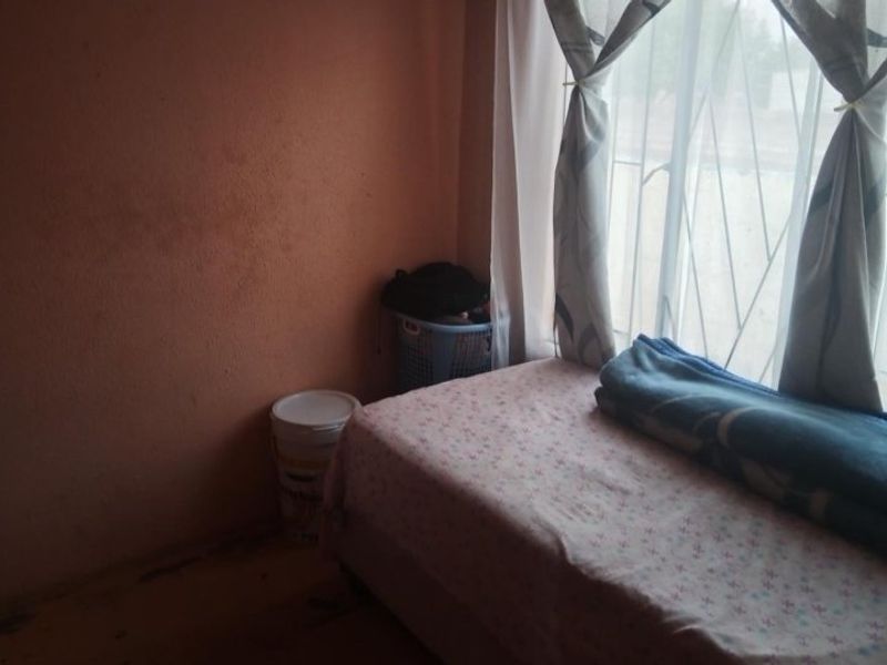 A bedroom featuring a window with security bars, requiring cosmetic updates to the walls and flooring to improve the overall condition.