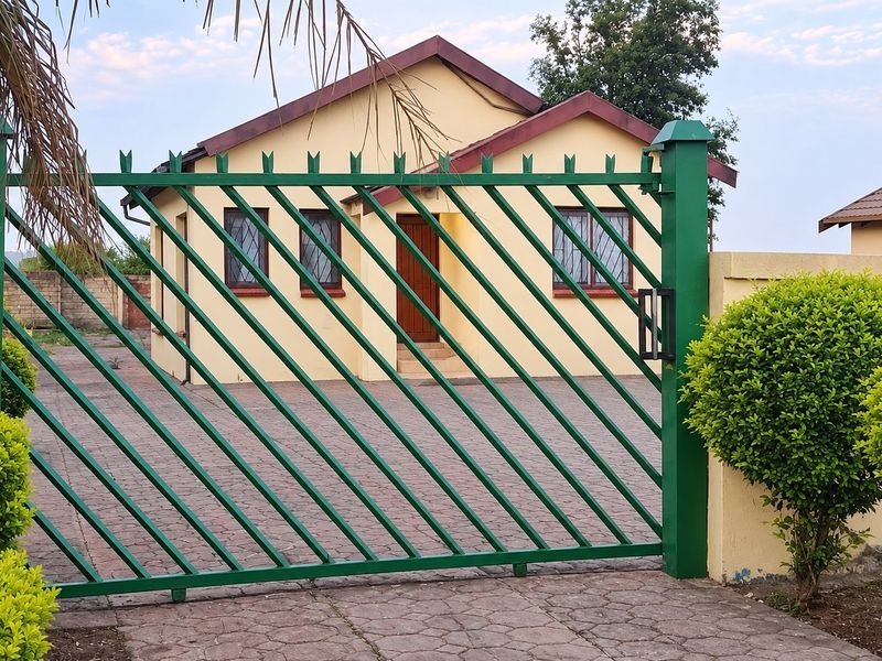 Front view of a residential house featuring a paved driveway, secure metal gate, and tiled roof, presented in a well-maintained condition.
