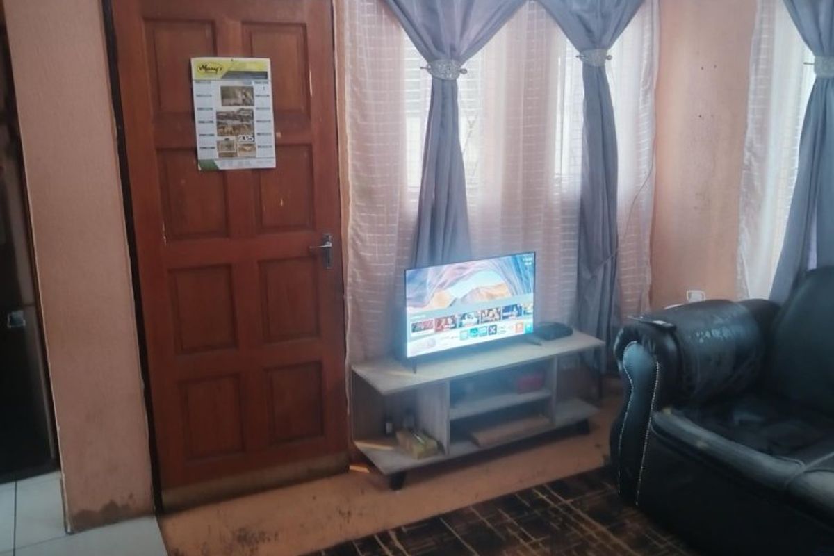A living room area featuring a timber door and window with curtains, showing signs of wear on the walls and flooring.