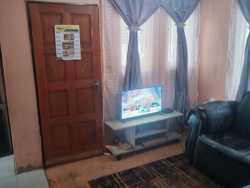A living room area featuring a timber door and window with curtains, showing signs of wear on the walls and flooring.