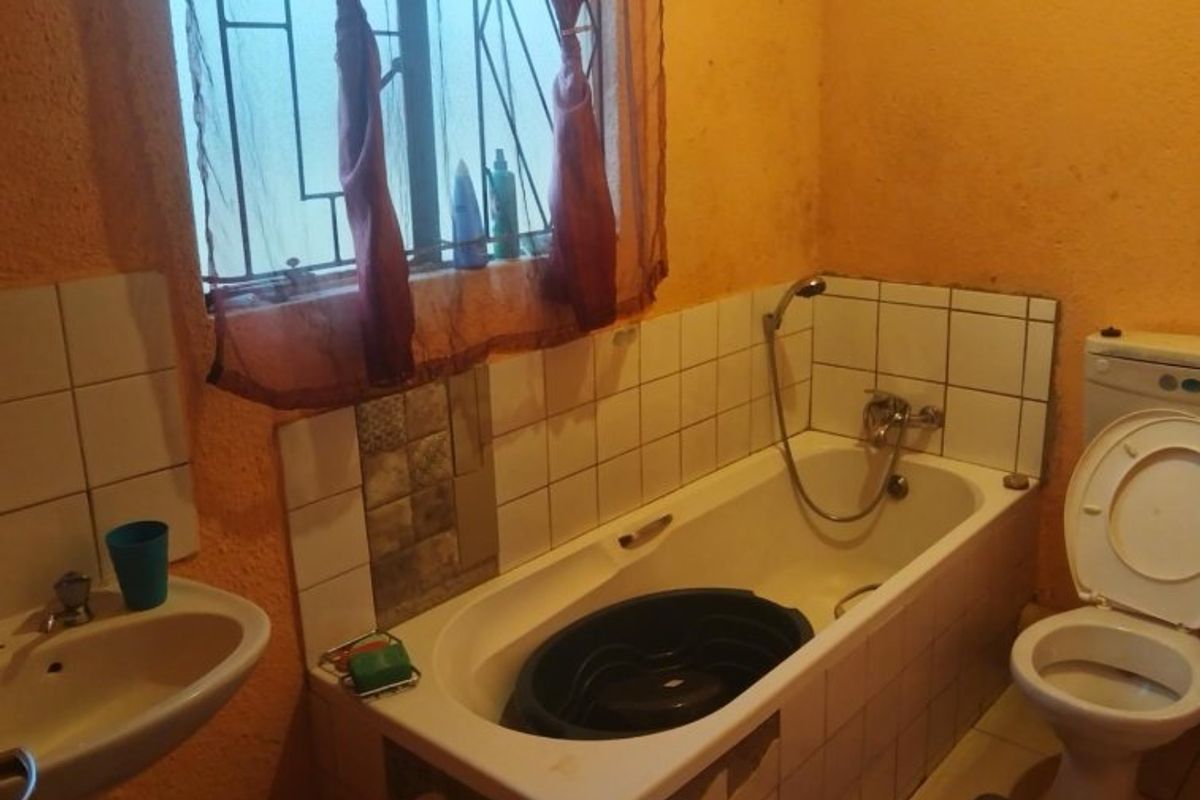 A functional bathroom featuring a bathtub with shower mixer, pedestal basin, and toilet, finished with tiled splashbacks and security bars on the window.