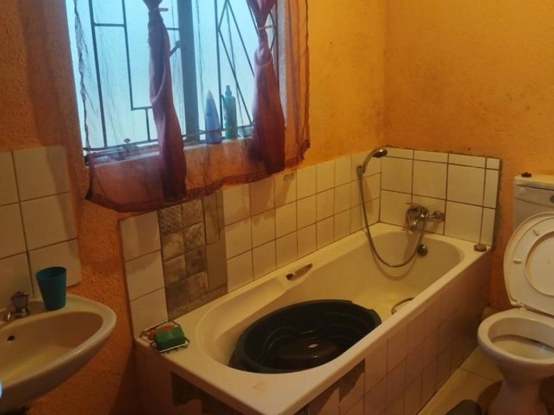 A functional bathroom featuring a bathtub with shower mixer, pedestal basin, and toilet, finished with tiled splashbacks and security bars on the window.