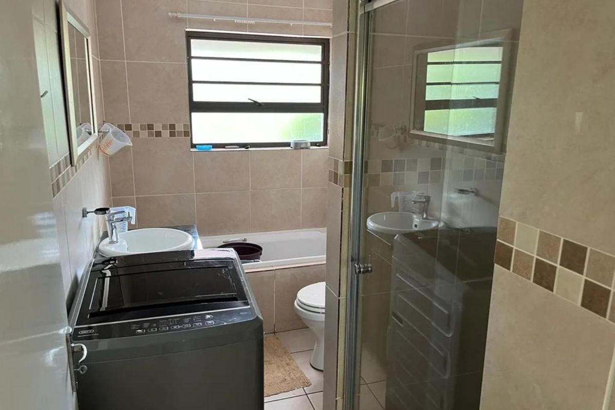 A functional bathroom featuring a shower enclosure, bathtub, toilet, and vanity basin with neutral wall and floor tiling.