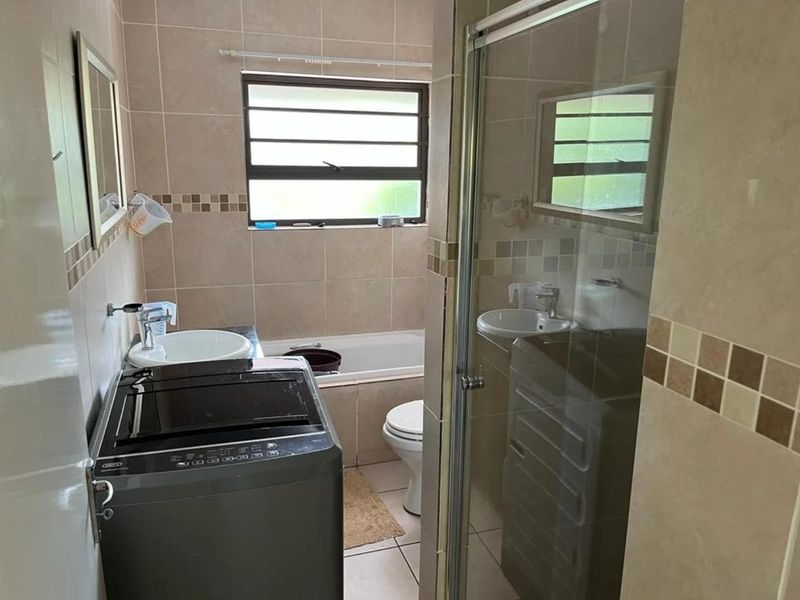 A functional bathroom featuring a shower enclosure, bathtub, toilet, and vanity basin with neutral wall and floor tiling.