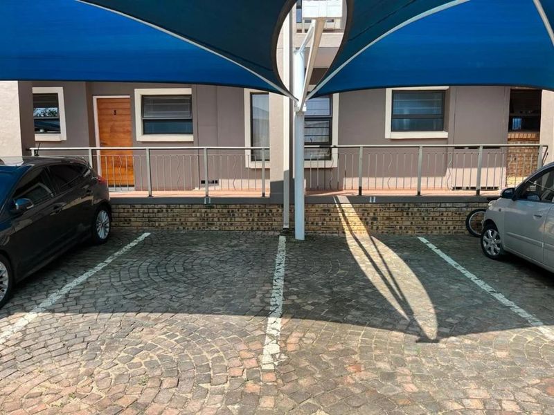 Front exterior view showing paved parking bays with a shade sail structure and access to the building entrance.