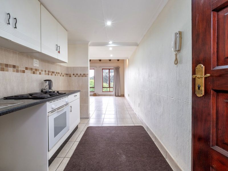 Open-plan kitchen area featuring built-in cabinetry, electric hob, and oven, leading into a bright living space with tiled flooring and recessed lighting.