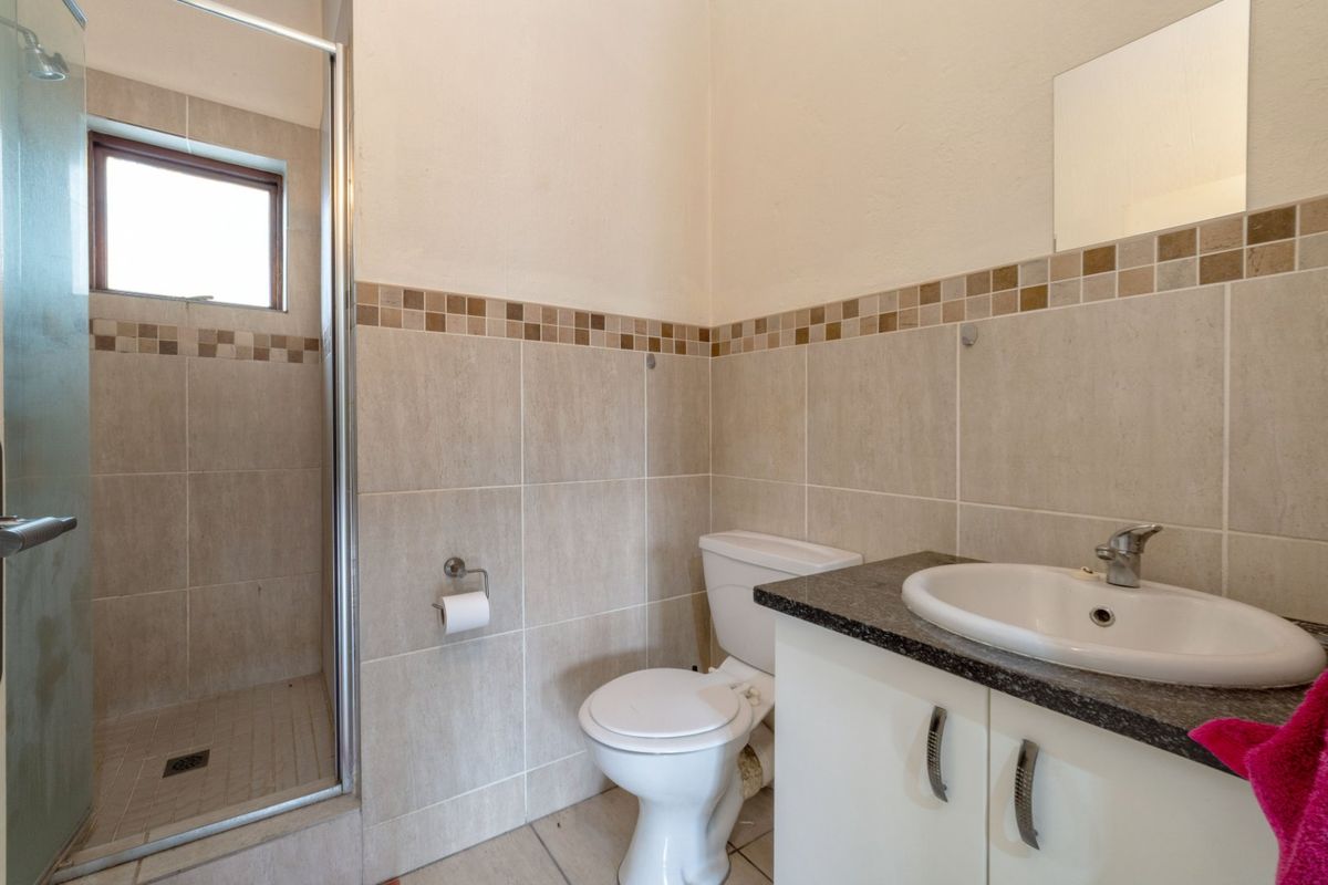 A functional bathroom featuring a shower enclosure, toilet, and a vanity cabinet with a basin, finished with neutral wall and floor tiling.