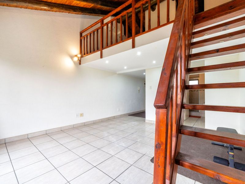Open plan living area featuring a wooden staircase leading to a mezzanine level, tiled flooring, and exposed timber ceiling beams.