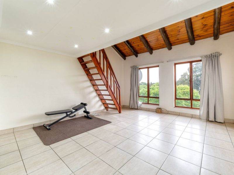 Spacious living area featuring tiled floors, exposed timber ceiling beams, and a wooden staircase leading to an upper level with large windows.