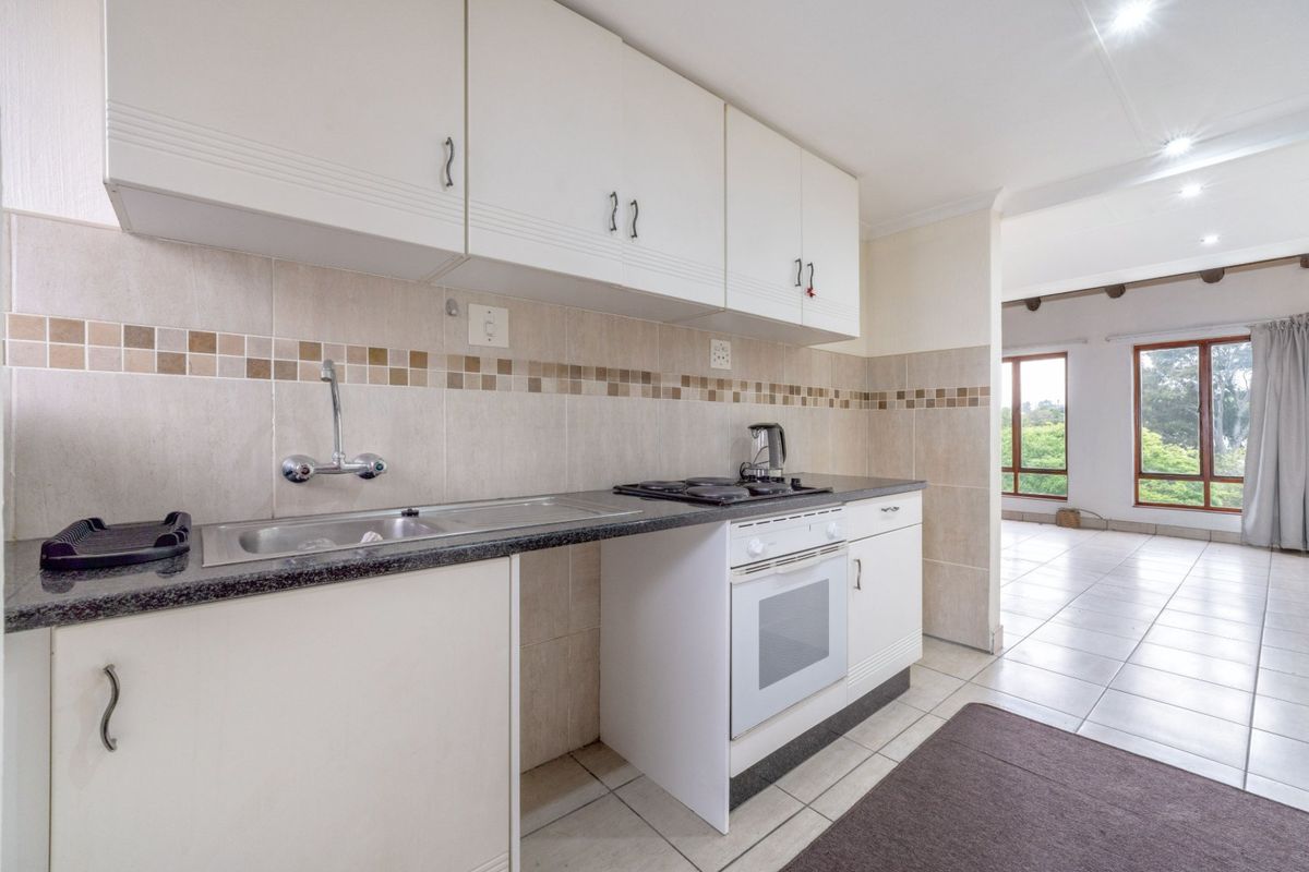 A functional kitchen featuring white cabinetry, a built-in oven and hob, tiled backsplash, and tiled flooring, flowing into an adjacent living area.