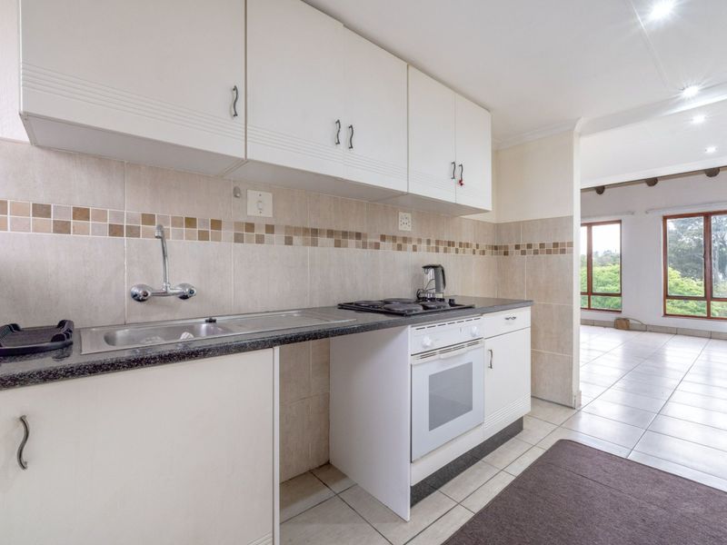 A functional kitchen featuring white cabinetry, a built-in oven and hob, tiled backsplash, and tiled flooring, flowing into an adjacent living area.
