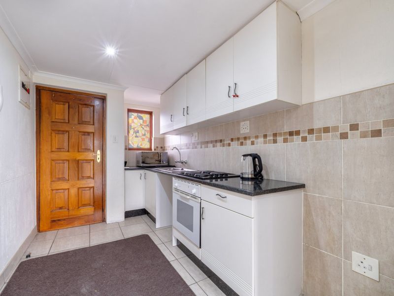 A functional kitchen featuring white cabinetry, granite countertops, a built-in oven, gas hob, and tiled backsplash with neutral floor tiles.