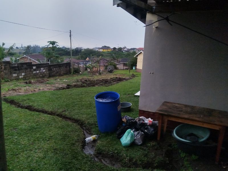 A view of the rear yard featuring a lawn, concrete block boundary wall, and roof overhang, showing signs of uneven ground and poor drainage.