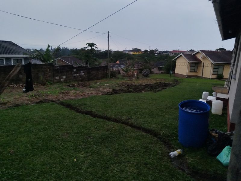 A view of the rear garden area featuring a lawn, boundary wall with security fencing, and surrounding residential properties.
