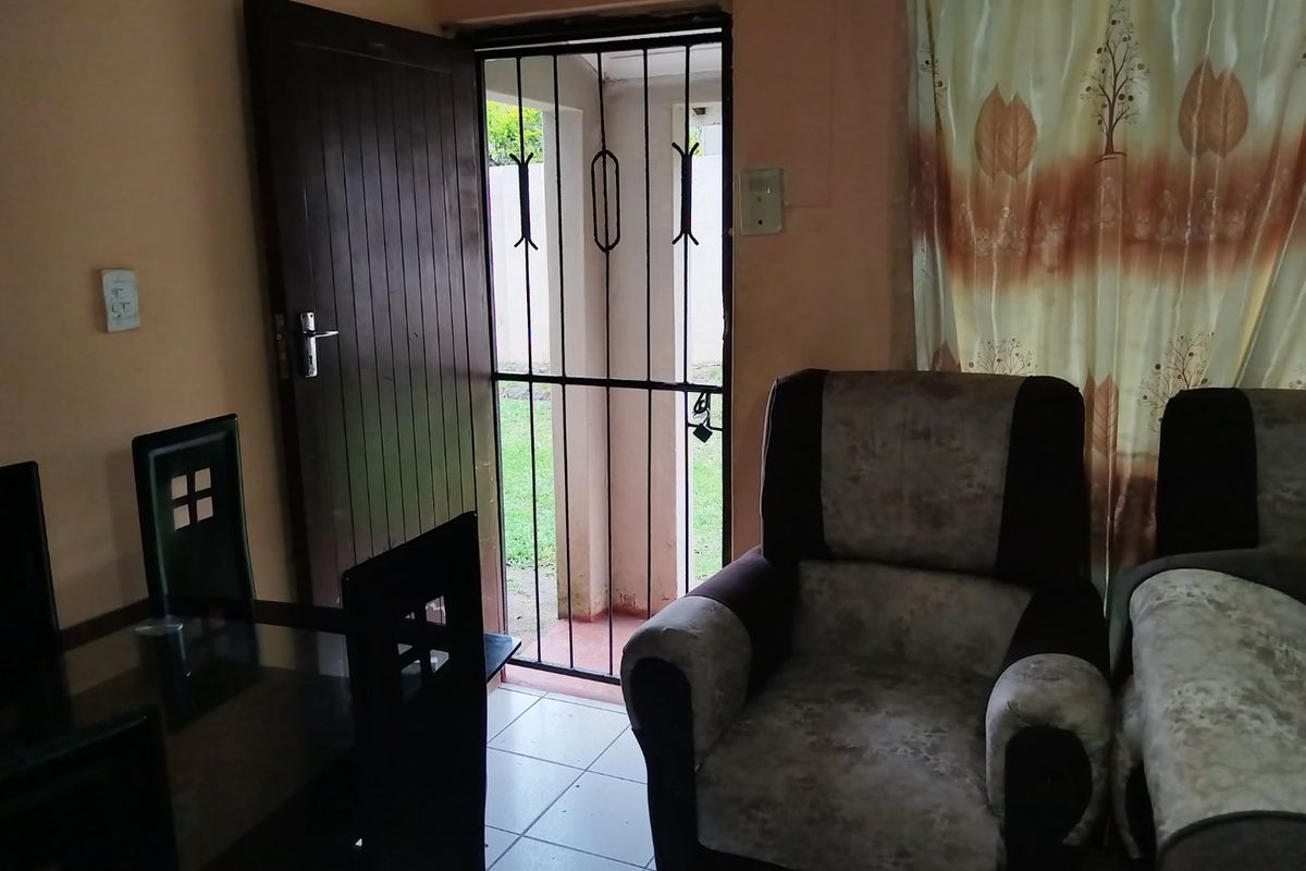 A living area featuring tiled flooring, a timber entrance door, and a security gate leading to the exterior.