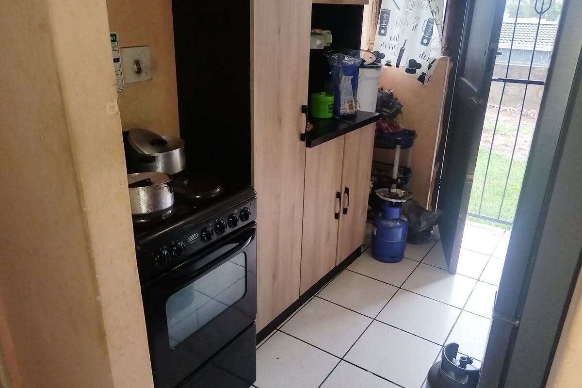A compact kitchen area featuring built-in cabinetry, a freestanding stove, and tiled flooring, with direct access to the exterior.