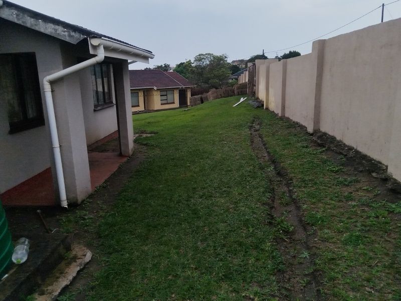 Rear exterior view showing a lawn area, boundary wall, and side access to the house with a rainwater downpipe.