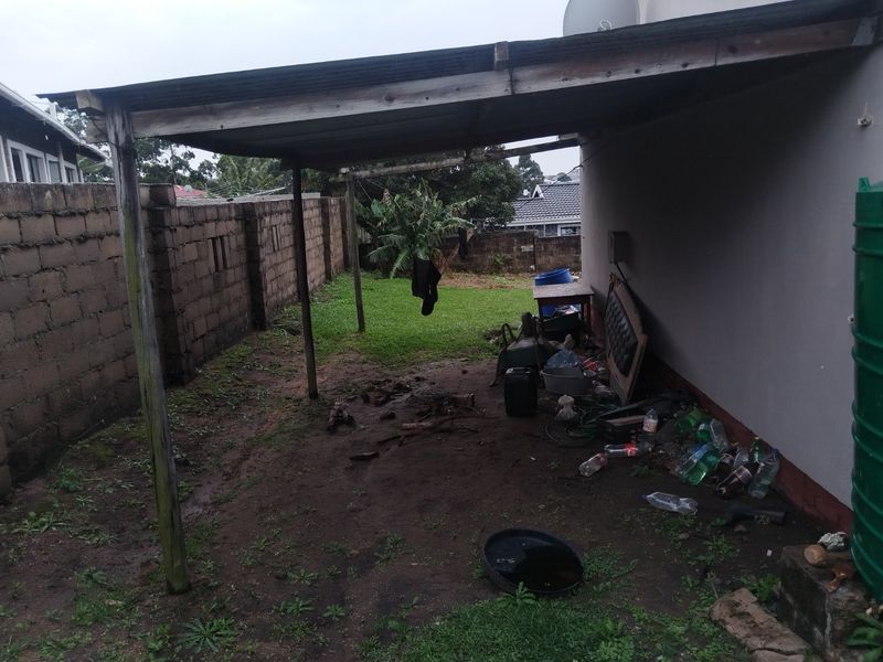 A covered outdoor patio area featuring a concrete block boundary wall and a water storage tank, requiring maintenance and landscaping improvements.