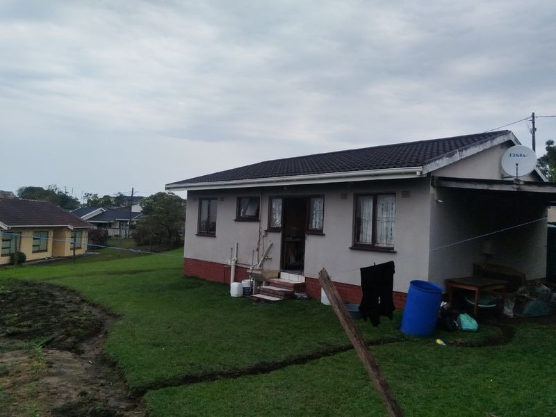 Rear view of a single-story house featuring a tiled roof, external sink, and a surrounding lawn area.