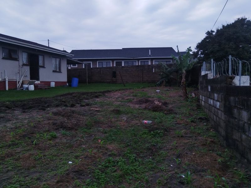 A rear exterior view of the property featuring a large, unlandscaped garden area enclosed by a concrete block boundary wall with razor wire.