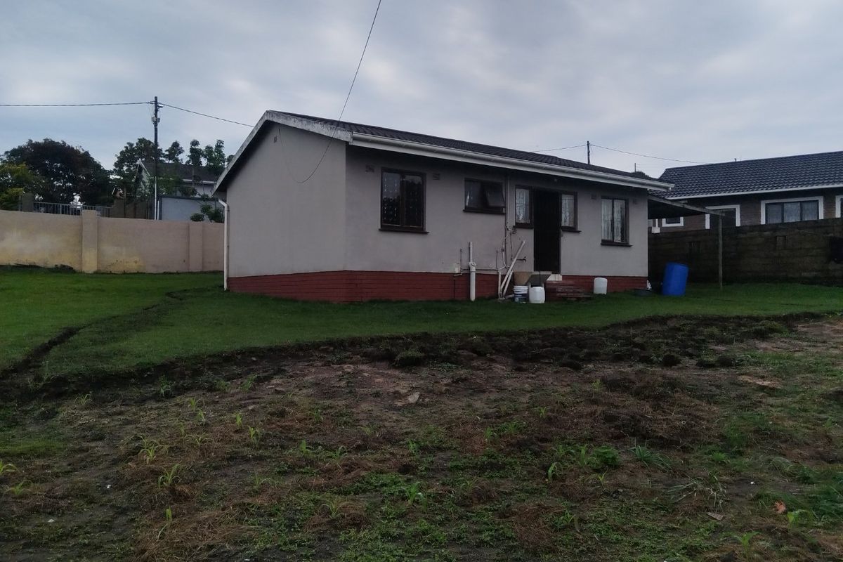 Rear view of a single-story detached house featuring plastered walls, a brick plinth, and a large garden area with exposed soil.