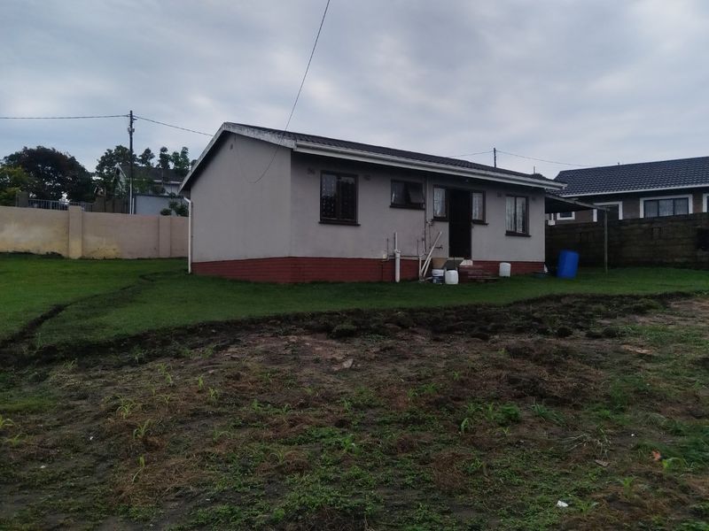 Rear view of a single-story detached house featuring plastered walls, a brick plinth, and a large garden area with exposed soil.