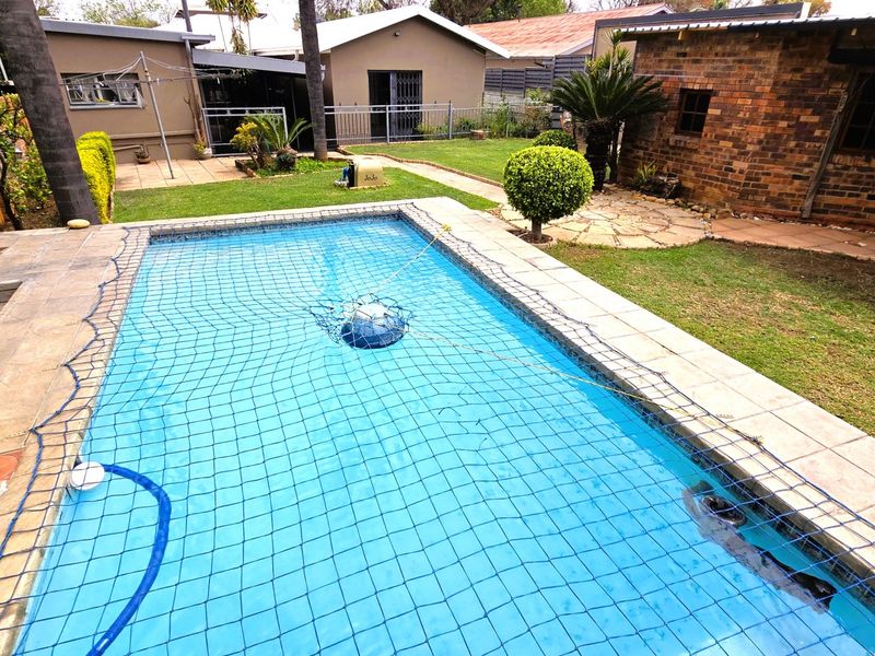 Outdoor pool area featuring a swimming pool with a safety net, paved surround, and a well-maintained garden with brick exterior walling.
