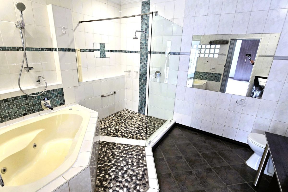 Spacious bathroom featuring a built-in bathtub, a separate glass-enclosed shower with pebble flooring, and neutral wall tiling.