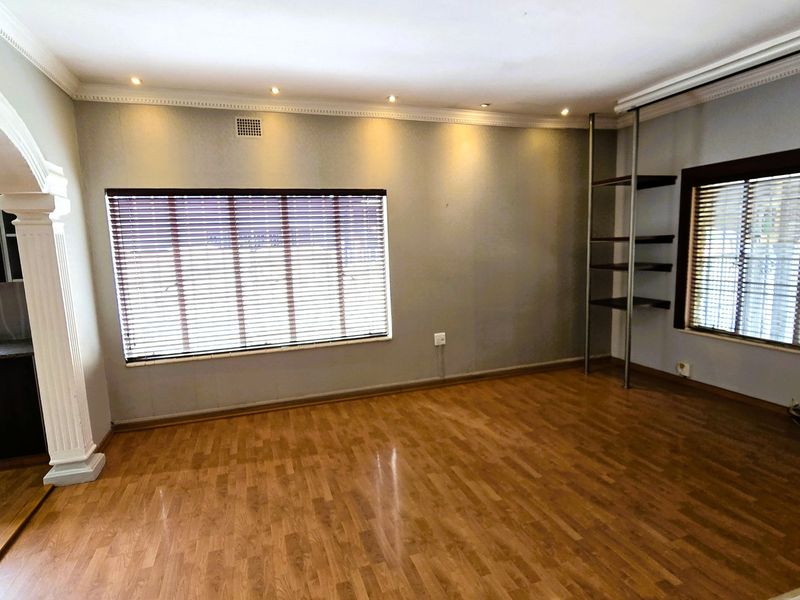 Spacious living area featuring laminate flooring, decorative cornicing, recessed lighting, and built-in shelving, with an open-plan flow to the adjacent kitchen area.