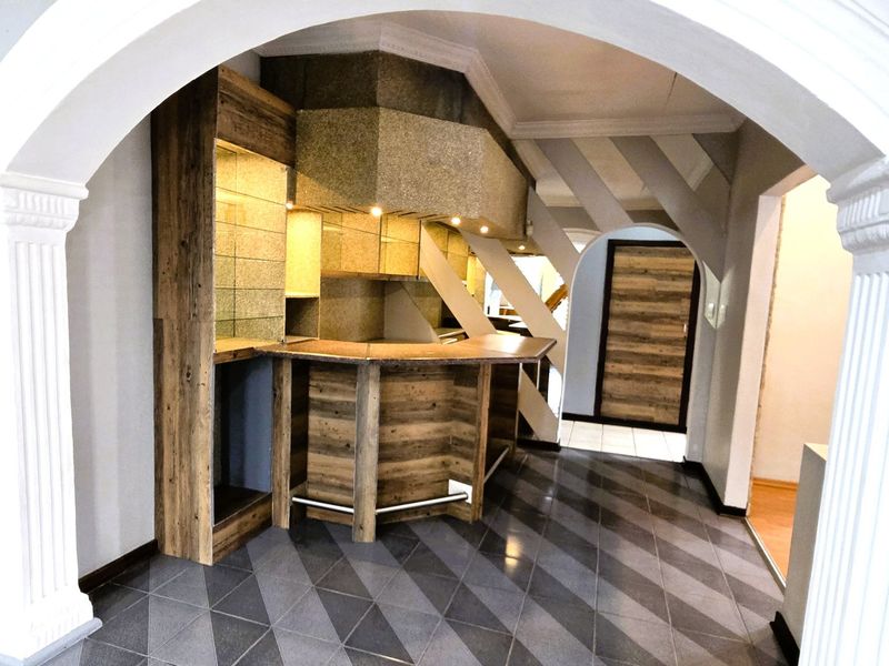A dedicated bar area featuring custom built-in cabinetry, a wooden bar counter, and decorative archways, finished with modern tiled flooring.