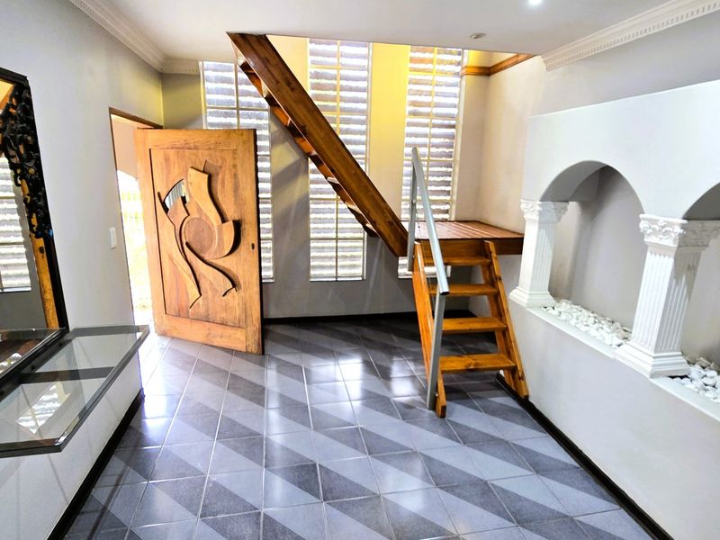 Spacious entry hall featuring a unique wooden staircase, decorative arched wall niche, glass block windows, and modern geometric tiled flooring.