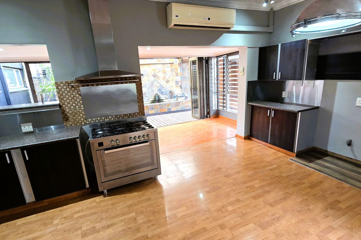 Spacious kitchen featuring dark cabinetry, gas stove with extractor, and laminate flooring, opening directly onto an outdoor patio area.
