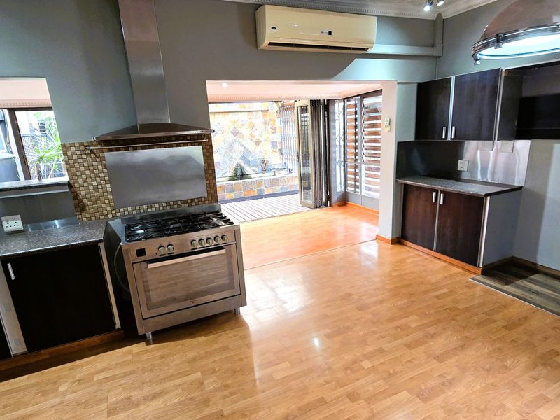 Spacious kitchen featuring dark cabinetry, gas stove with extractor, and laminate flooring, opening directly onto an outdoor patio area.